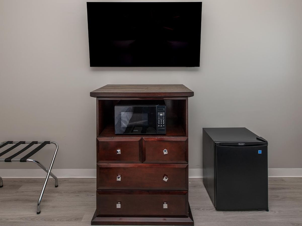Wooden dresser with microwave, TV, small fridge, and a luggage rack.