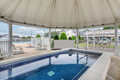 Covered hot tub overlooking pool and landscaped grounds under a cloudy sky at Ogunquit Hotel