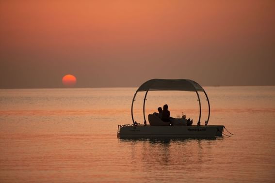 A couple sits in a boat on the water with the golden light of a beautiful sunset near Grand Park Kodhipparu, Maldives