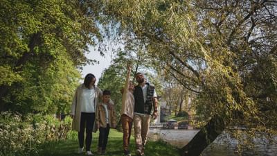 Family of four stands together by a lake under trees with a boy pointing upwards.