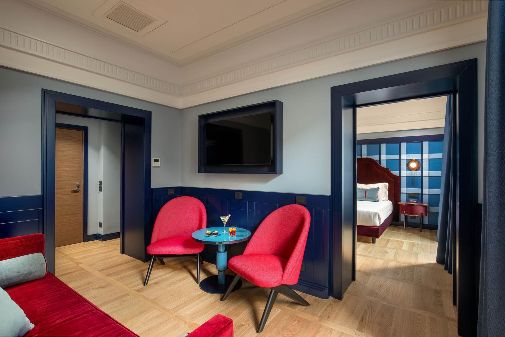Stylish Cielo Suite at The Independent with two red chairs, a round table, a wall-mounted TV, and bedroom view
