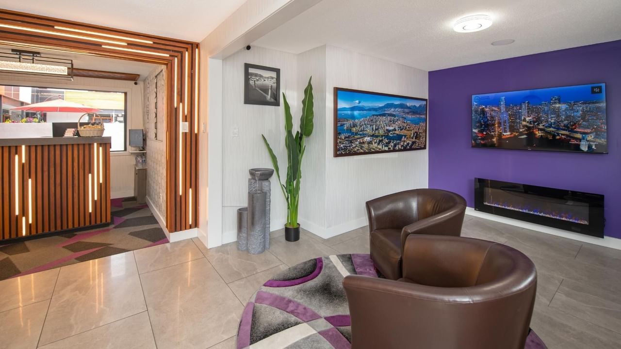 Hotel lobby with brown chairs, purple walls, fireplace, and city view on screens.