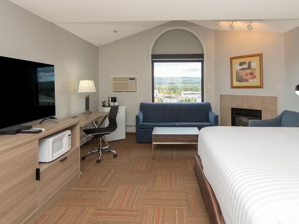 Spacious suite with king bed, blue sofa, work desk, fireplace, and arched window.