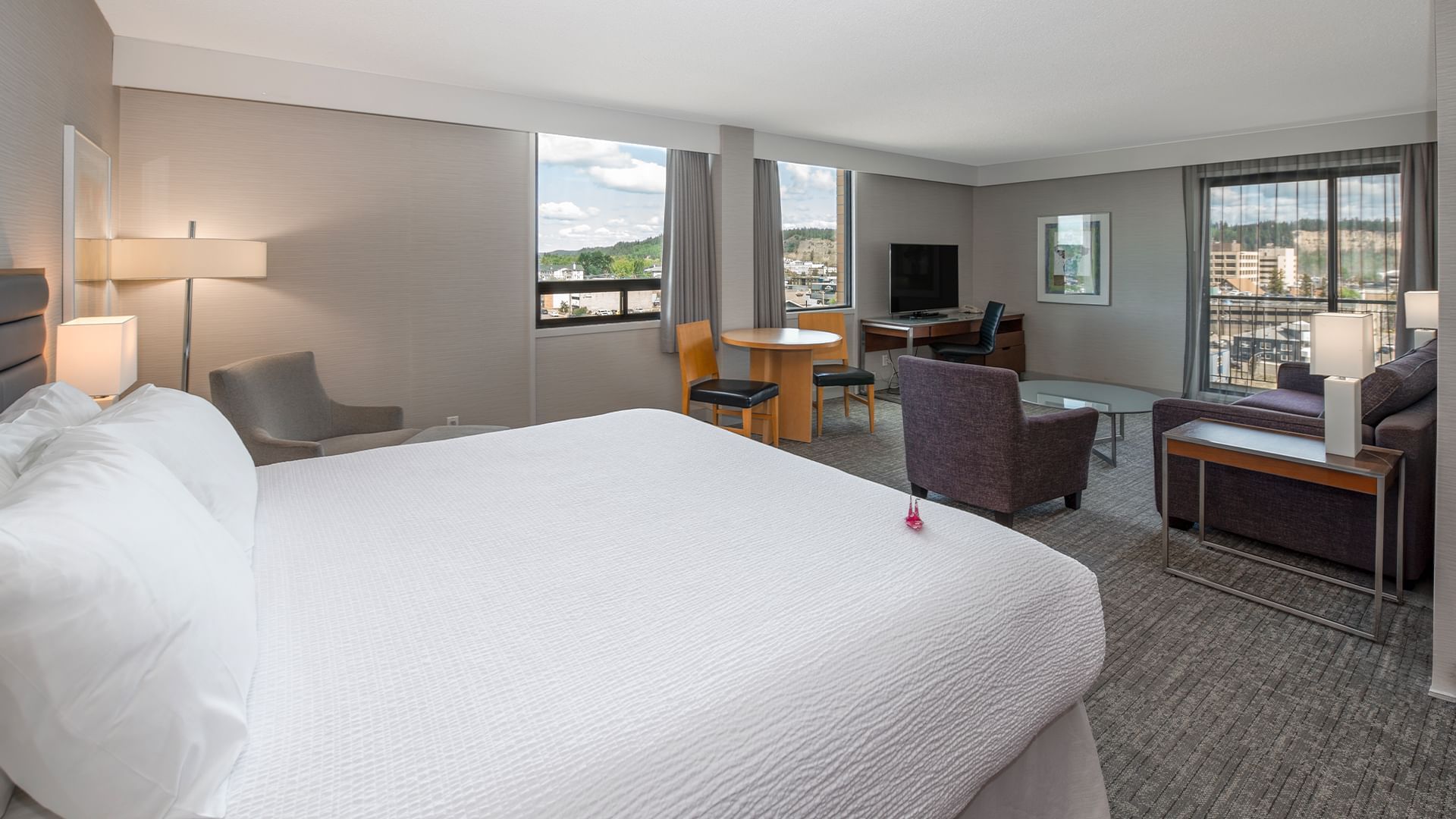 A hotel room with a large bed, seating area, and a view of the city.