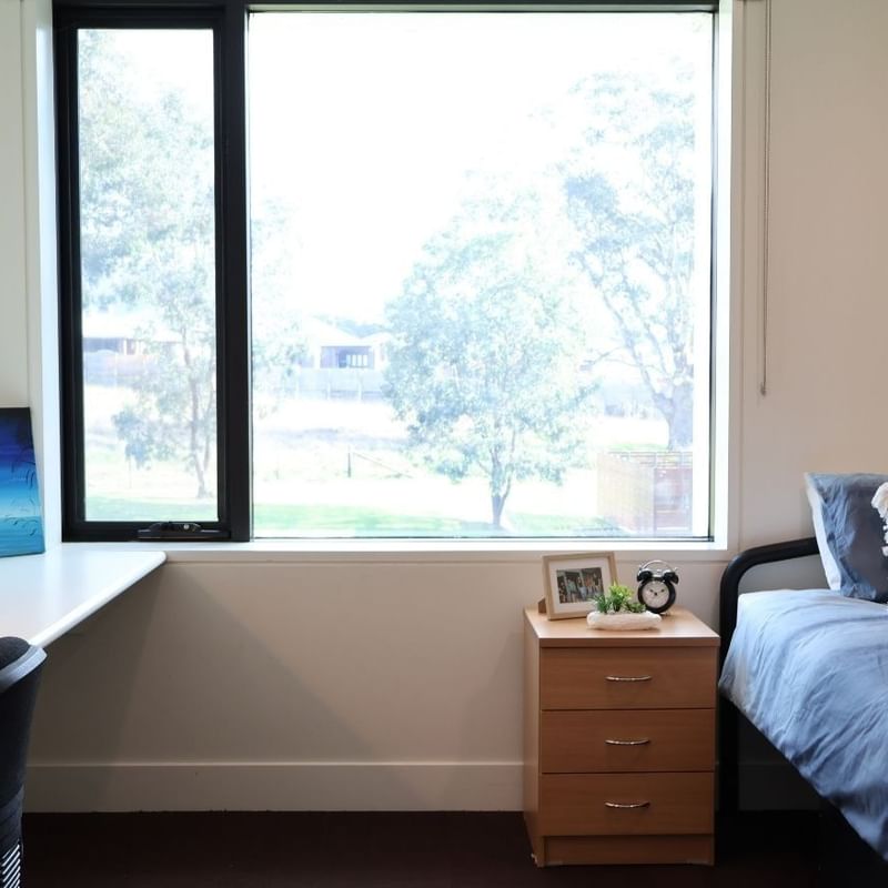 A clean room with a bed, desk, bookshelf, and window at La Trobe University - McFarlane's Hill Residences.