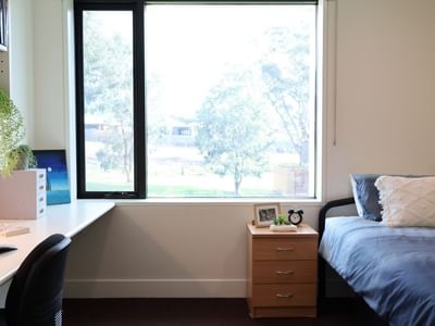A clean room with a bed, desk, bookshelf, and window at La Trobe University - McFarlane's Hill Residences.