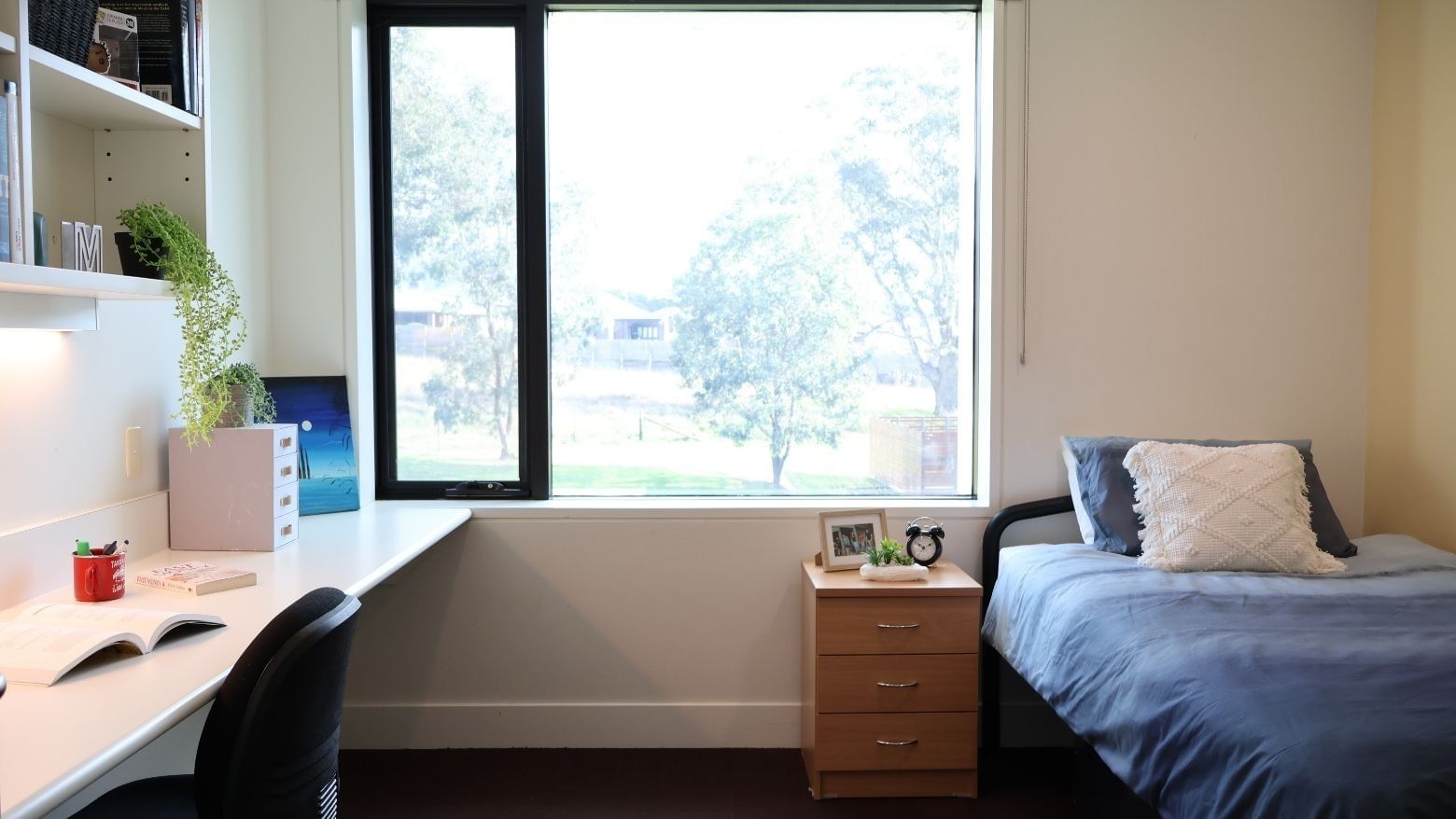 A clean room with a bed, desk, bookshelf, and window at La Trobe University - McFarlane's Hill Residences.