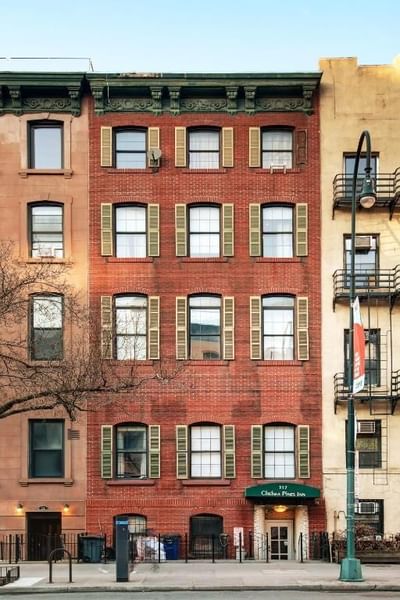 Chelsea Pines Inn building with many windows and green shutters, adjacent to a street with a sign and lamp post.