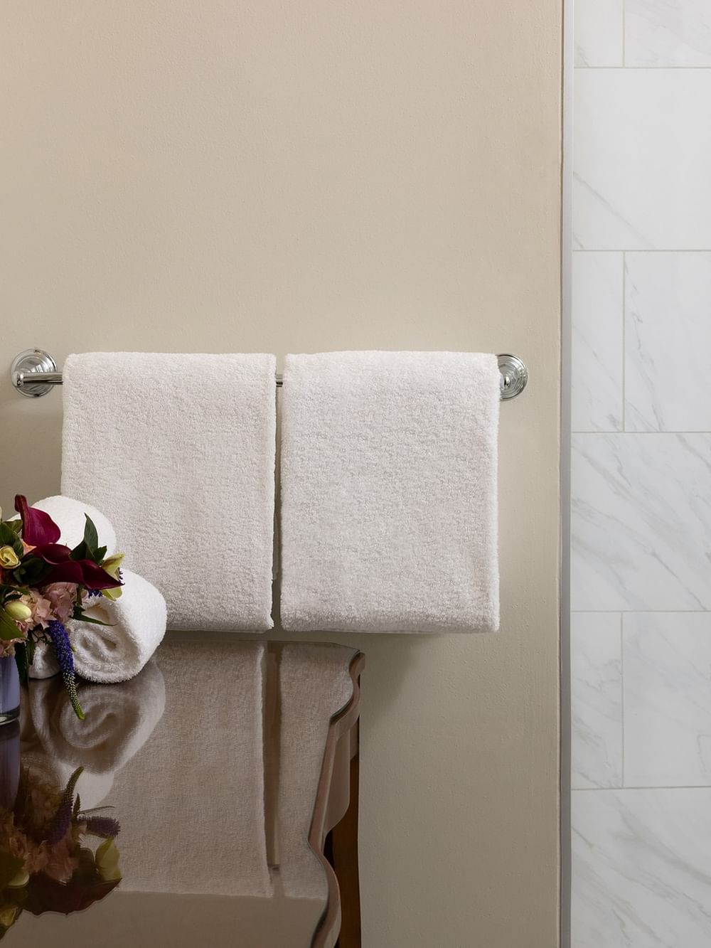 White towels, flower arrangement, and toiletries on a table beside a bathroom shower at Warwick Melrose Dallas.