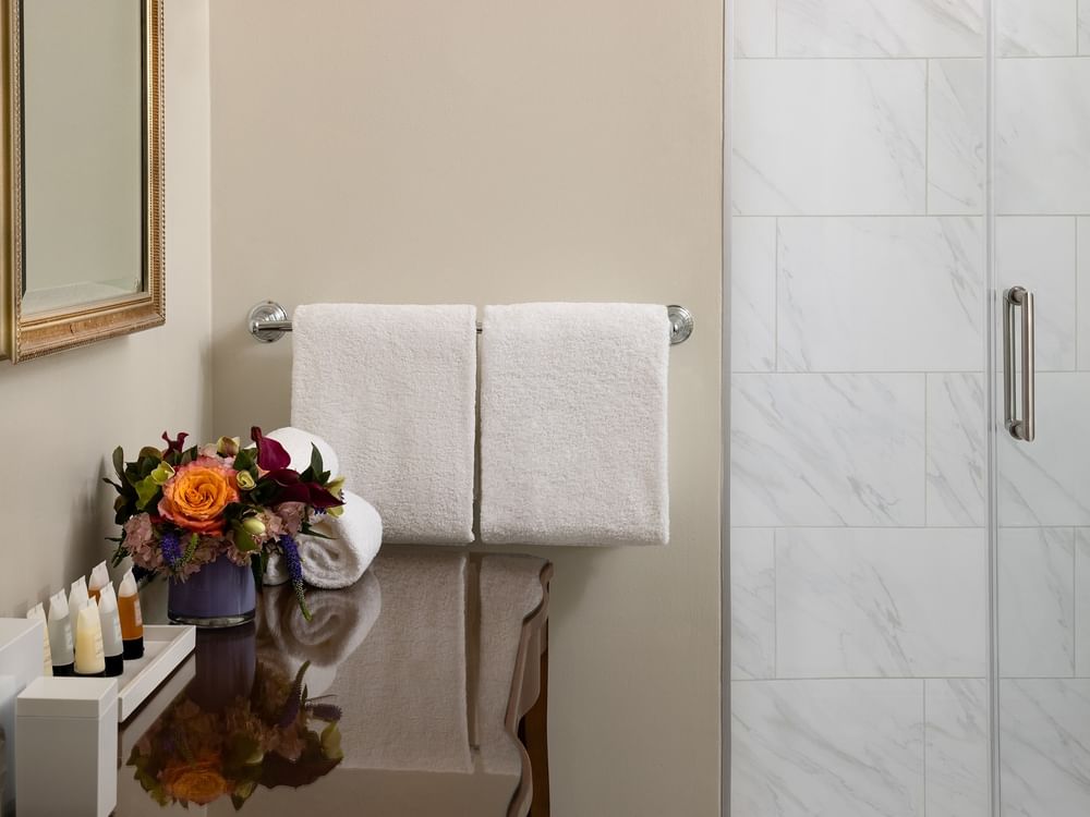 White towels on a silver rack by a marble shower wall under a gold-framed mirror in Classic Double at Warwick Melrose Dallas