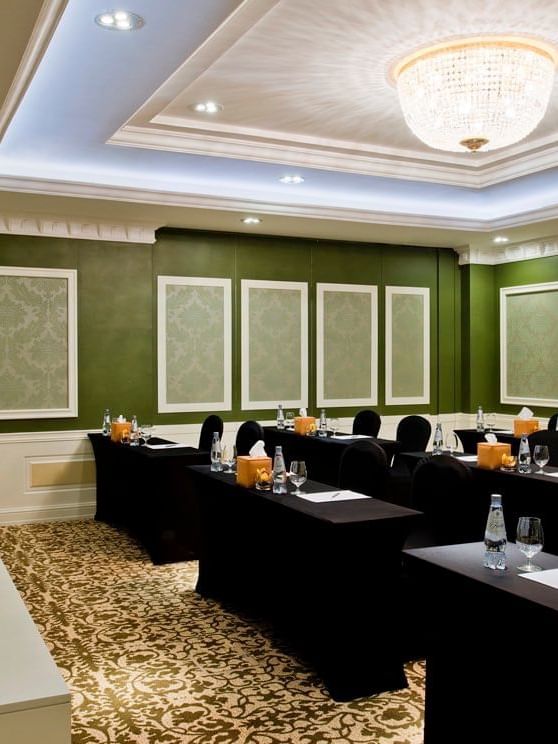 Emerald Room features black chairs by long tables under a crystal chandelier with green walls at Warwick Doha Hotel