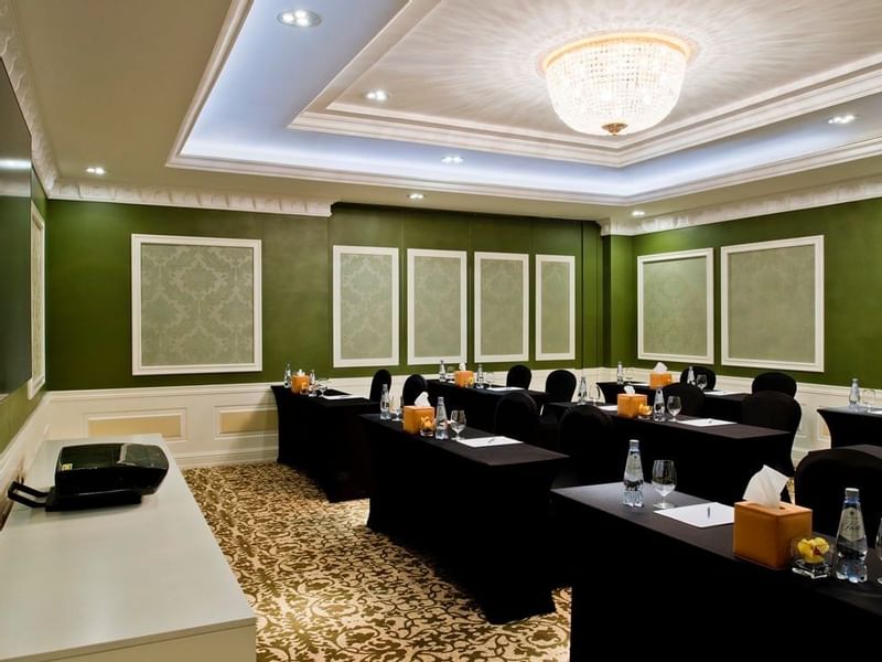 Emerald Room features black chairs by long tables under a crystal chandelier with green walls at Warwick Doha Hotel