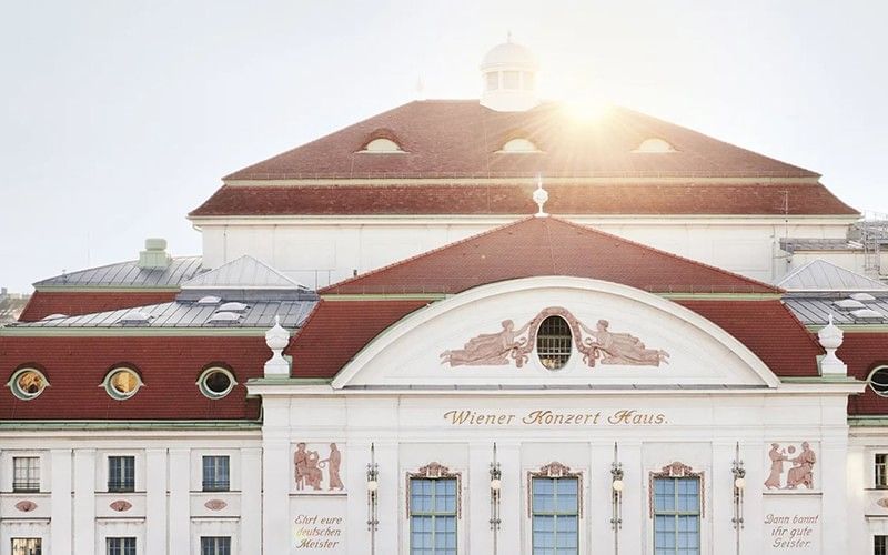 Historische Fassade des Wiener Konzerthauses mit rotem Ziegeldach und dekorativen Stuckelementen im warmen Sonnenlicht.