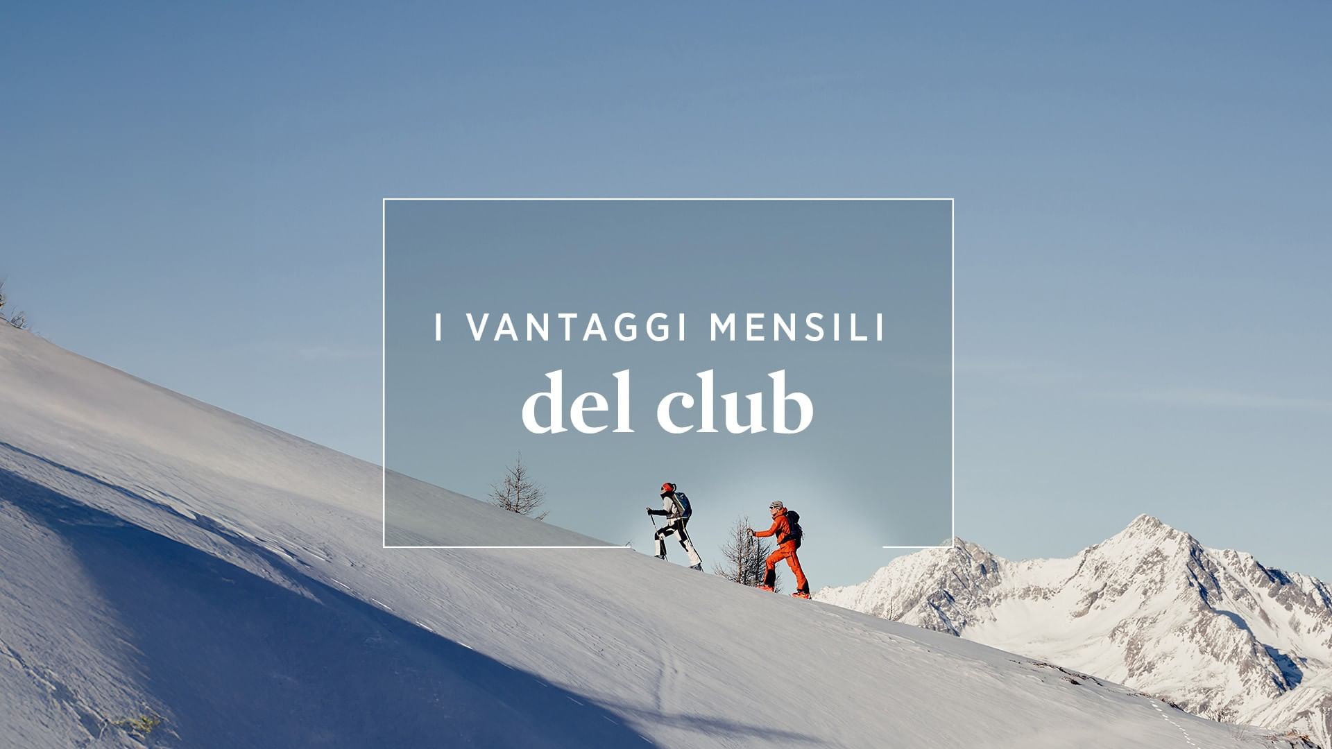 Due persone camminano su un pendio innevato con montagne innevate sullo sfondo.