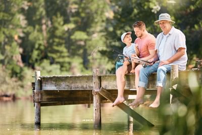 Happy father, grandfather, and child fishing together on a wooden dock in a lake near Fall Creek Marina & Campground