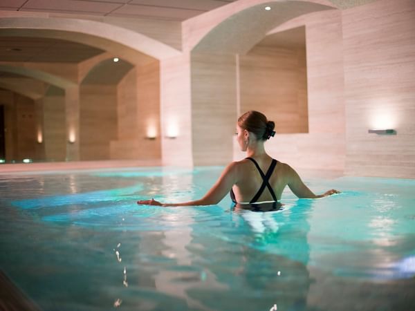 Kvinna kopplar av i upplyst inomhuspool med elegant arkitektur och mjuk belysning i spa-miljö