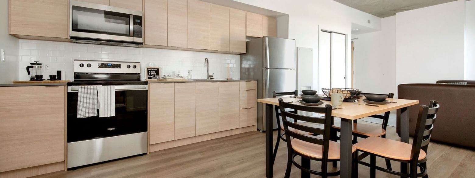 A modern and full sized kitchen with stainless steel appliances and a kitchen table with four seats.