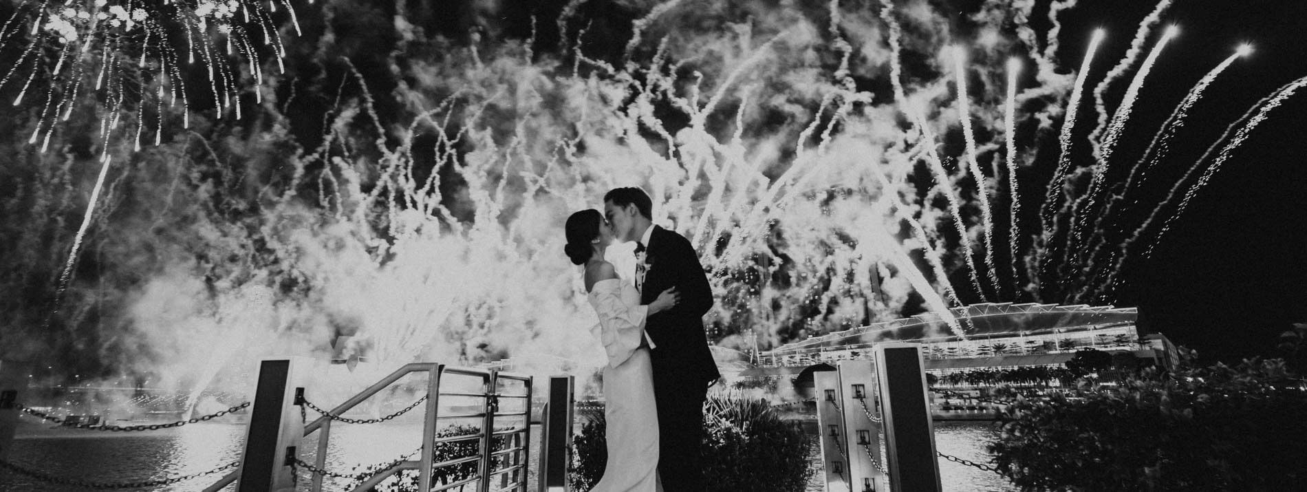 Black and white images of a wedded couple kissing under fireworks at The Fullerton Hotels and Resorts