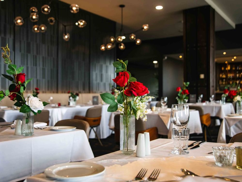 Elegant dining room with set tables, white tablecloths, and centerpieces of red and white flowers.