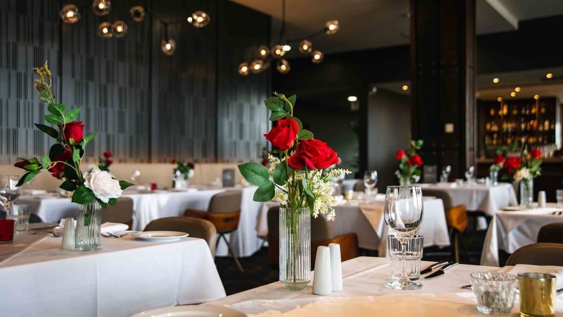 Elegant dining room with set tables, white tablecloths, and centerpieces of red and white flowers.