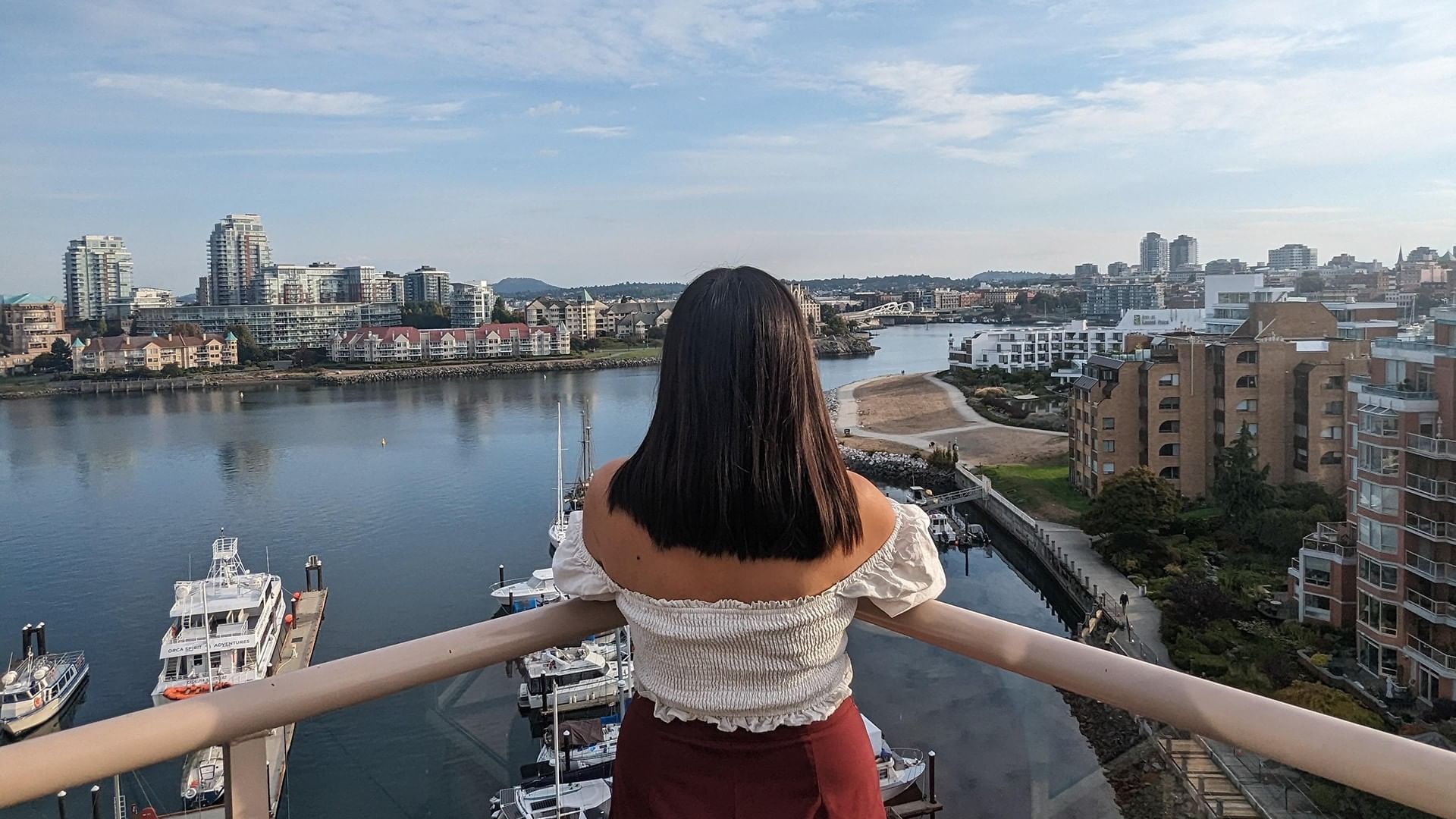Woman on balcony overlooking marina and cityscape at Coast Victoria Hotel & Marina by APA