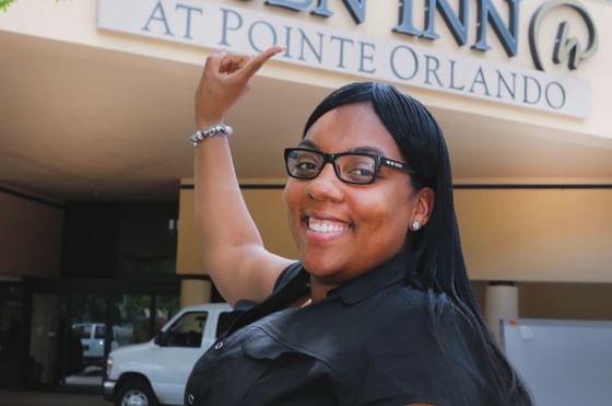 Laquandra Terry pointing towards main entrance building logo with white car in driveway at Rosen Inn at Pointe Orlando