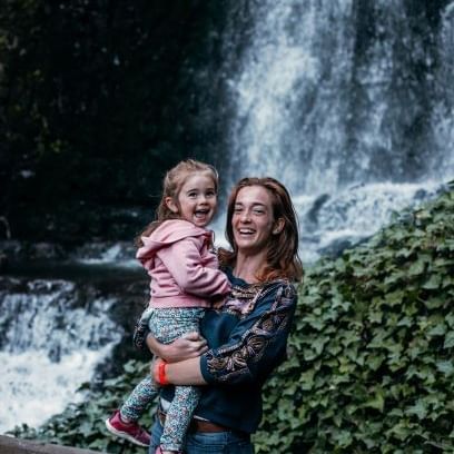 A lady carrying a kid by the waterfall near DOT Hotels
