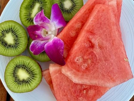 Plate of watermelon slices and kiwi halves garnished with a purple flower on a wooden table.