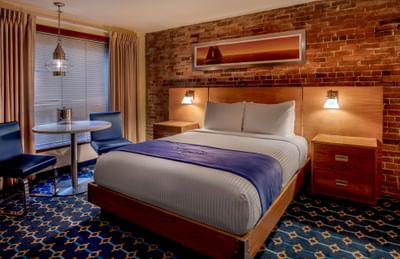 Bed with sailboat art above the headboard next to a window and table in Queen Atrium View at Harborside Inn Boston