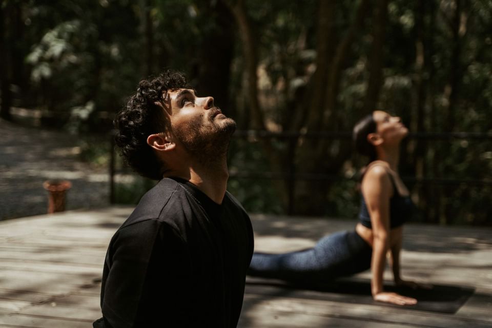 Two people practice yoga on a wooden deck surrounded by greenery at The Dwarika's Himalayan Wellbeing