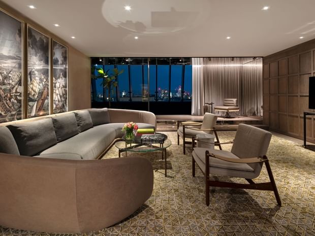 Elegant lounge with a curved sofa and city night views in Signature Suite at The Londoner Hotel