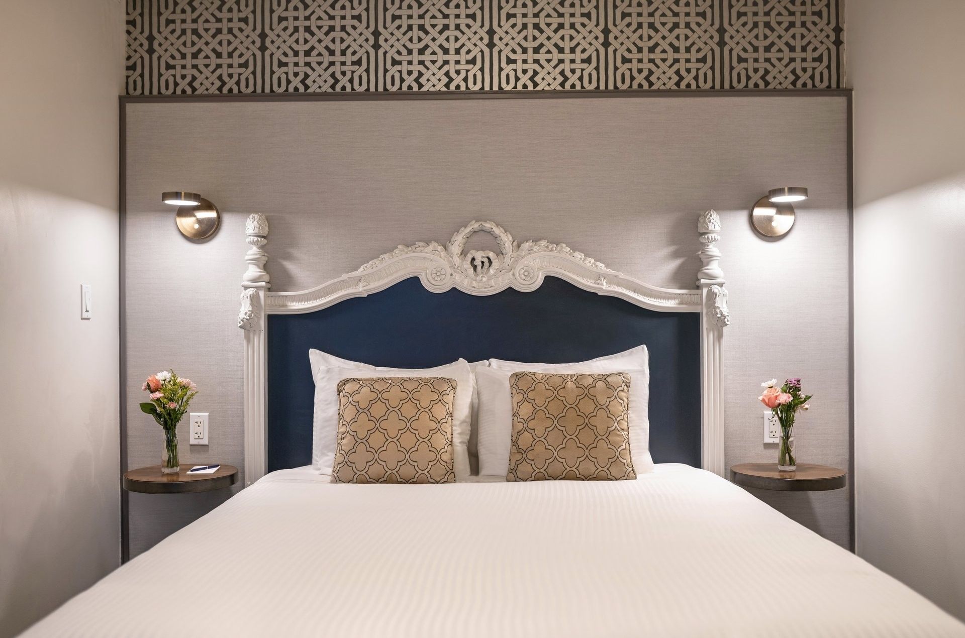 Bed with an ornate headboard by floating nightstands under brass lamps in Suite at Warwick San Francisco