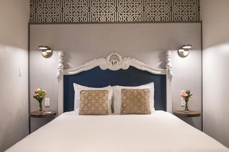 Bed with an ornate headboard by floating nightstands under brass lamps in Suite at Warwick San Francisco