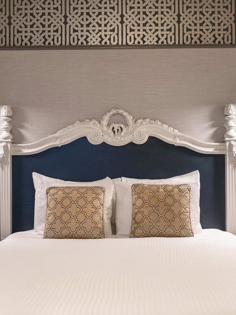 Bed with an ornate headboard by floating nightstands under brass lamps in Suite at Warwick San Francisco