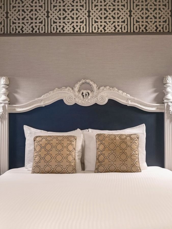 Bed with an ornate headboard by floating nightstands under brass lamps in Suite at Warwick San Francisco
