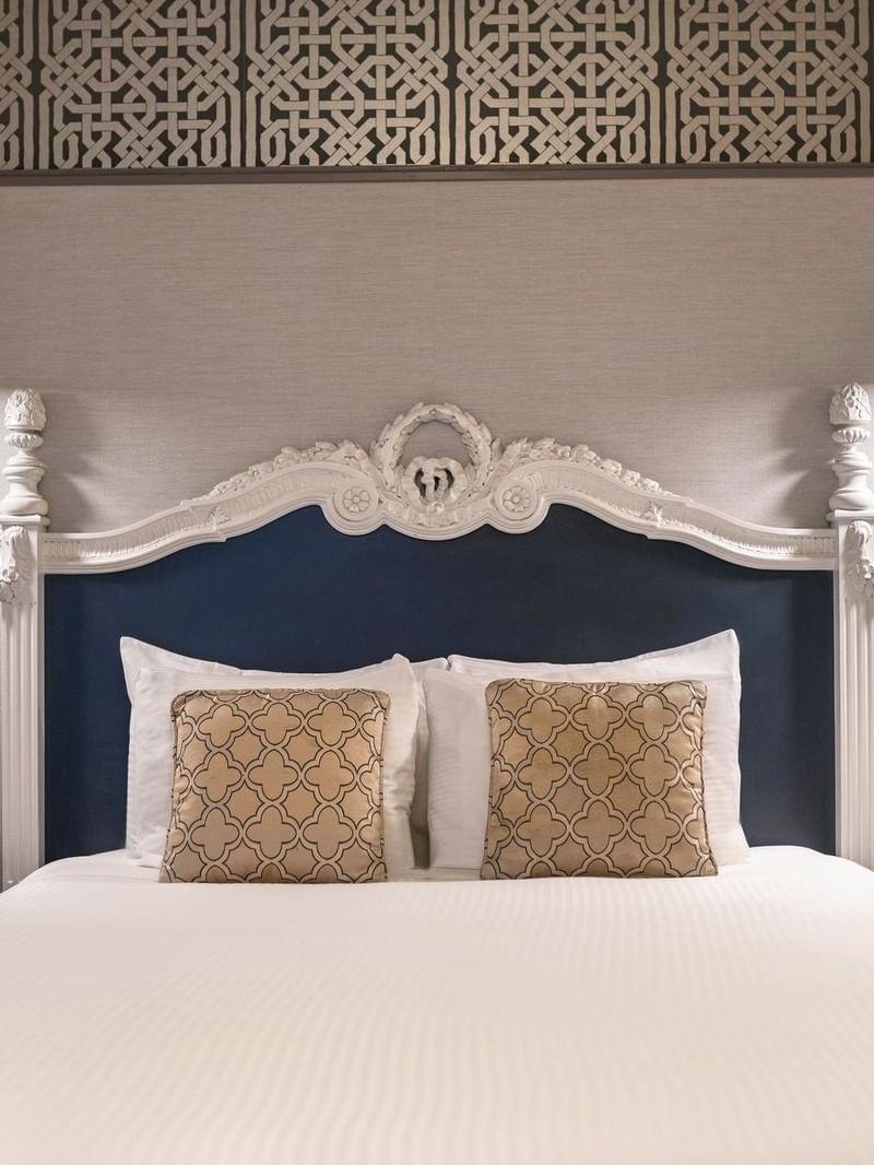 Bed with an ornate headboard by floating nightstands under brass lamps in Suite at Warwick San Francisco