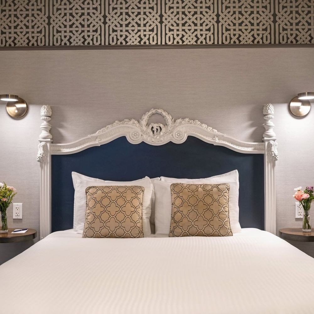 Bed with an ornate headboard by floating nightstands under brass lamps in Suite at Warwick San Francisco