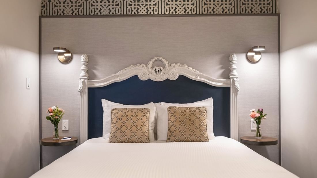 Bed with an ornate headboard by floating nightstands under brass lamps in Suite at Warwick San Francisco