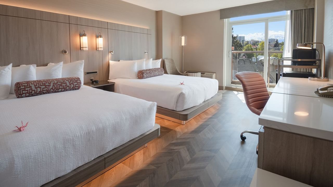 Hotel guestroom with two queen beds, work desk, and balcony