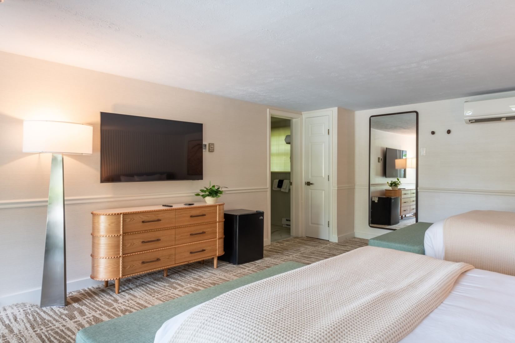 A hotel room with two beds, a dresser, TV, and mirror.
