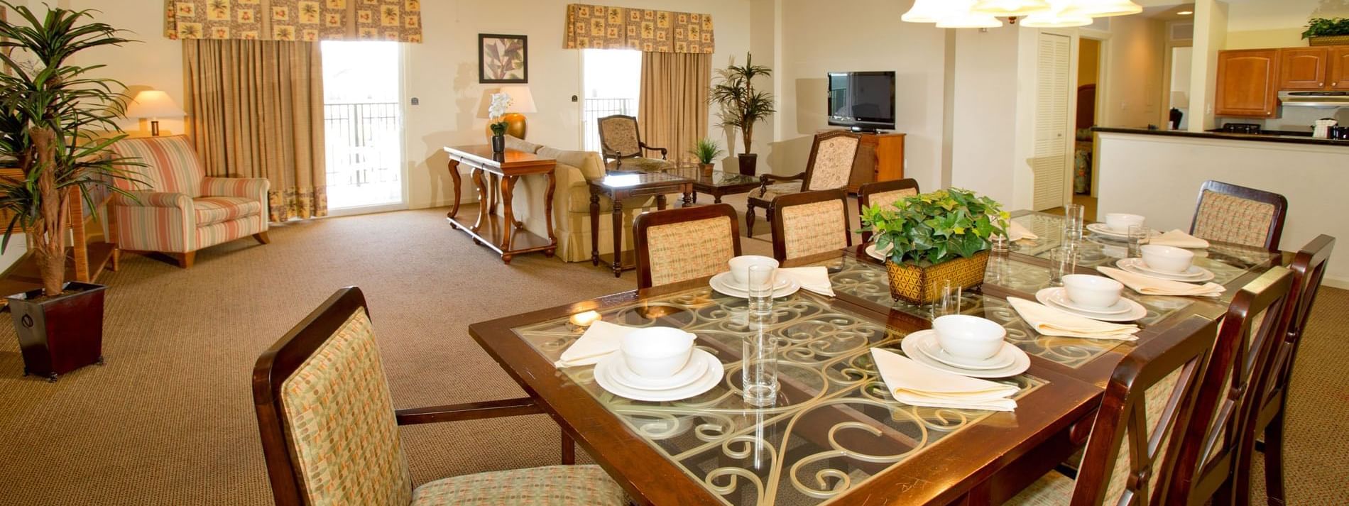 A wide view of a suite with a dining table, living area, kitchenette, and balcony access.