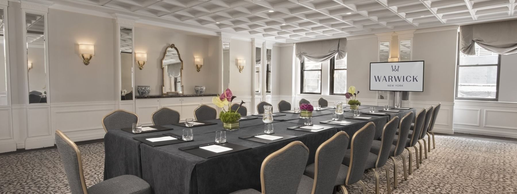 Rectangular boardroom table set facing large TV with water glass in Oxford meeting room at Warwick New York