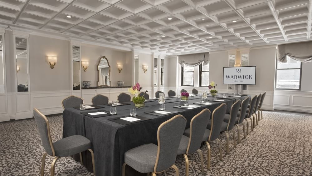 Rectangular boardroom table set facing large TV with water glass in Oxford meeting room at Warwick New York