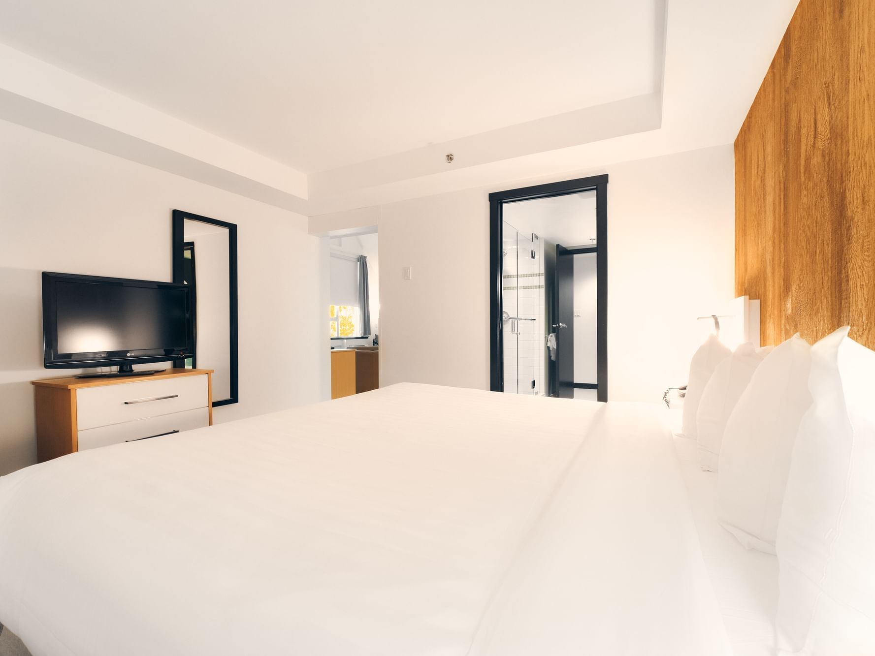 Executive Suite room at Paradox Aava Whistler Hotel with white bed with three pillows, and wooden dresser with TV.