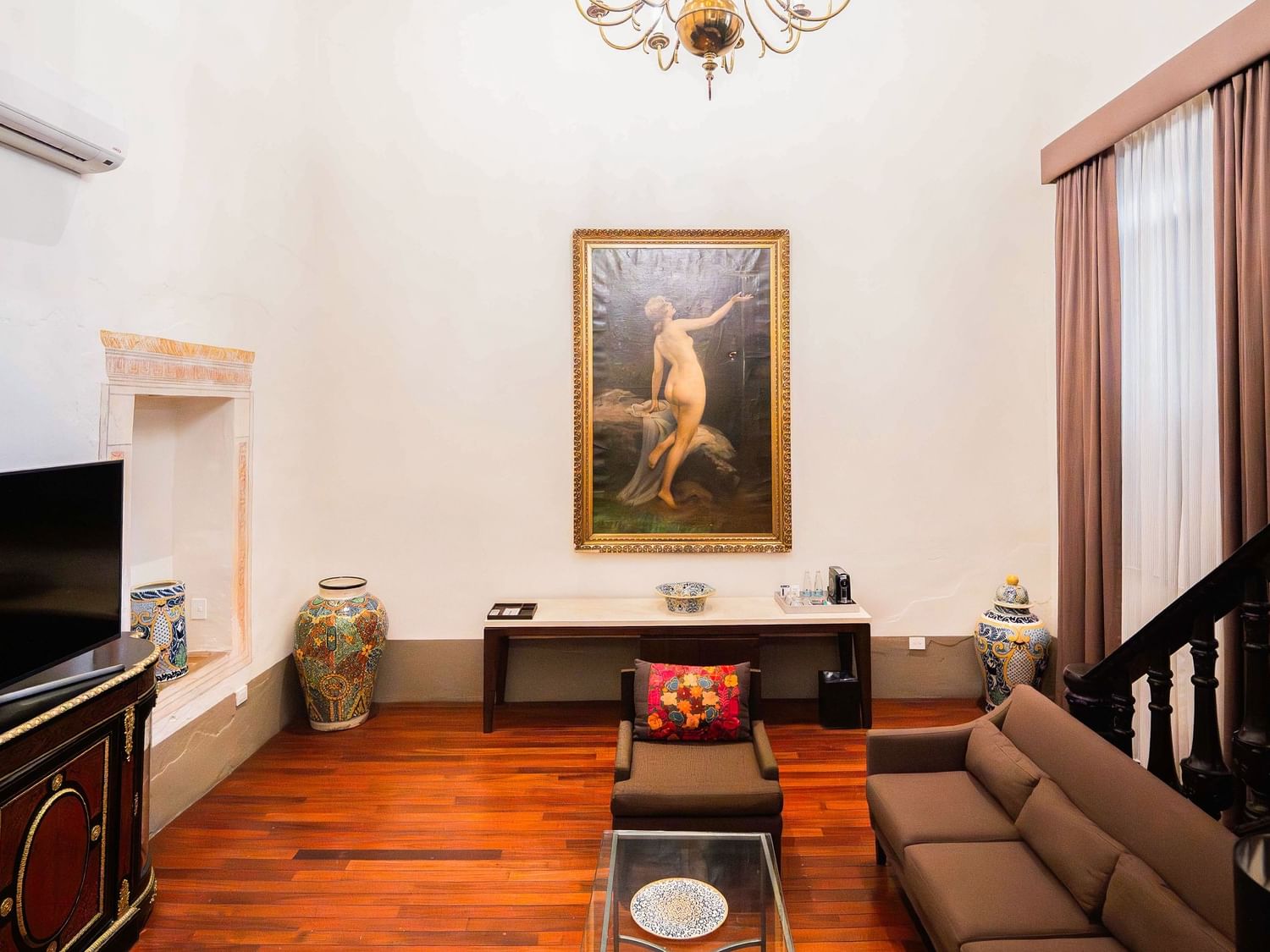 Salón elegante con sofás, televisión, cuadro y escalera en Suite Presidencial King de Quinta Real Puebla en Heroica Puebla de Zaragoza