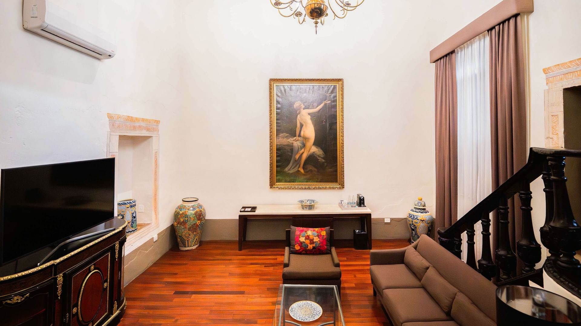 Salón elegante con sofás, televisión, cuadro y escalera en Suite Presidencial King de Quinta Real Puebla en Heroica Puebla de Zaragoza