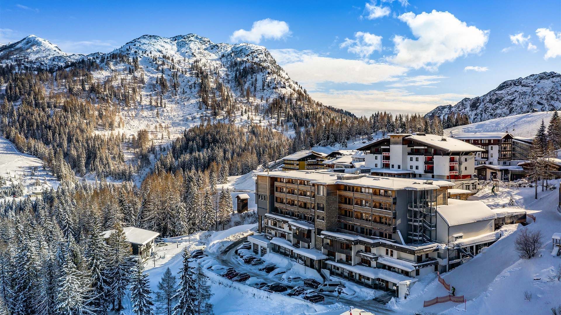 Snow-covered Falkensteiner Hotel Sonnenalpe with pine trees and mountain peaks 