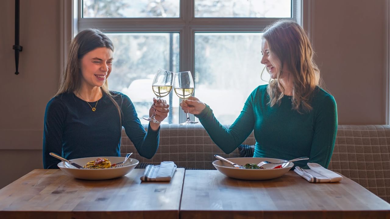 Two friends in a Canmore restaurant smile and cheers their wine glasses during a mid week getaway.