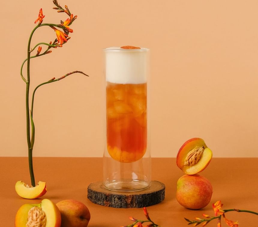 Peach layered drink surrounded by fresh peaches and flowers, served in the Park Lounge at Park Hyatt Saigon