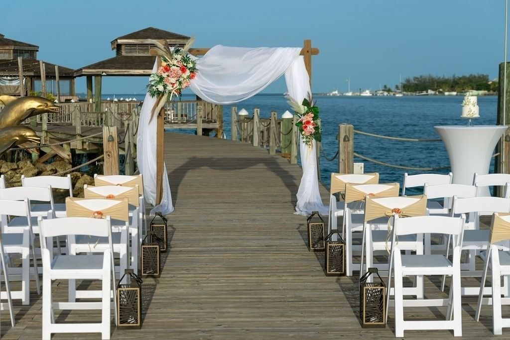 White floral wedding arch by rows of chairs under a blue sky on a wooden pier at Warwick Paradise Island Bahamas